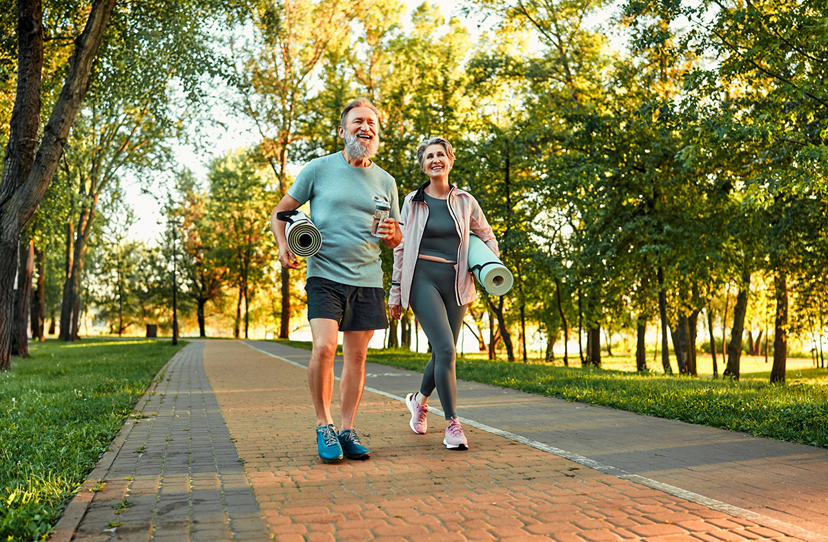 Man and woman walking to outdoor yoga session through a park